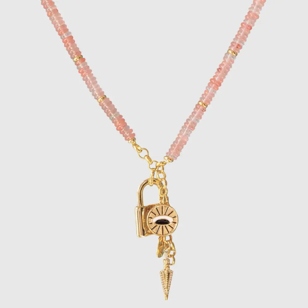 Pink gemstone beaded necklace with gold spiritual charms including padlock, evil eye and pointed talisman on light background